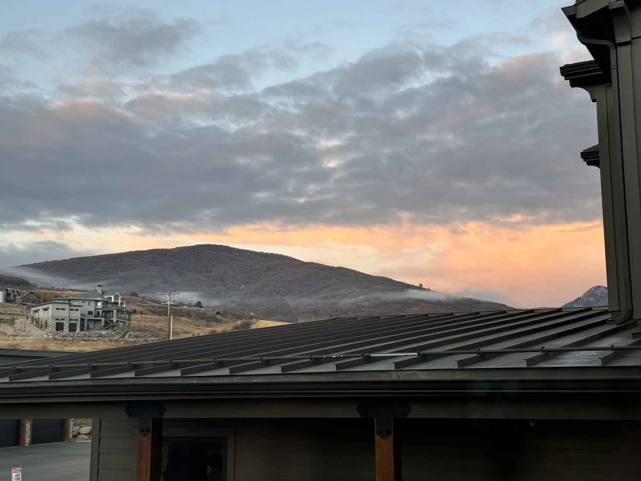 A standing-seam roof beneath a glowing sky and mountain hillside